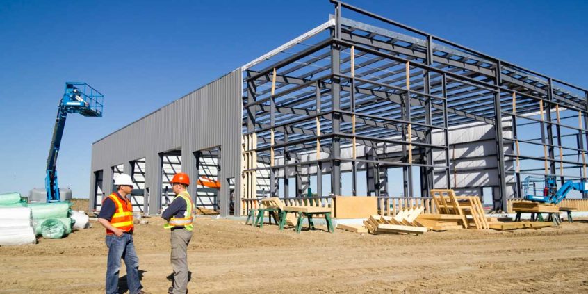 Construction workers discussing warehouse construction cost for a PEMB building
