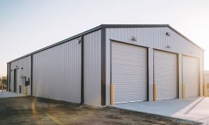 40x75 metal building garage with three roll-up doors, gray steel siding, black trim, and a concrete driveway