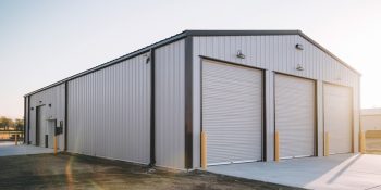 40x75 metal building garage with three roll-up doors, gray steel siding, black trim, and a concrete driveway