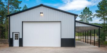 30x60 farm shop metal building with an attached lean-to, black and white steel siding, a roll-up door, and a side entry, set in a wooded area