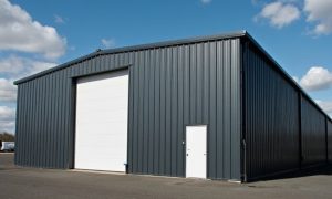 40x75 prefab steel building with dark gray steel siding, tall white roll-up door, and side entry on a paved surface
