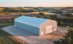40x70 white metal building barn with a gambrel roof, roll-up door, and side entry, set on a rural farm with rolling hills in up state New York