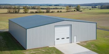 80x80 metal building with light gray PBR siding and a paved driveway, set in open farmland