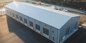 Auto repair shop / garage metal building (50x120) with multiple bays, gray PBR panel siding, and a paved lot near a highway