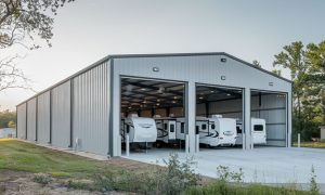 Large commercial metal building being used for RV storage with three open bays, painted gray with multiple RVs parked inside