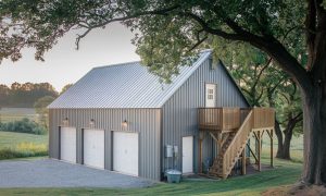 Three-car metal building garage with a loft, in gray and white and an exterior staircase leading to a wooden deck in Washington state.