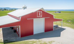 Red metal barn with a side lean-tos, a cupola, and gravel drive, set in open farmland with mountain views, Portland Oregon