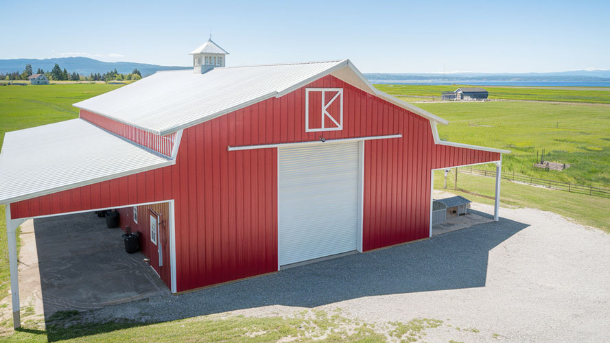 Red metal barn with a side lean-tos, a cupola, and gravel drive, set in open farmland with mountain views, Portland Oregon