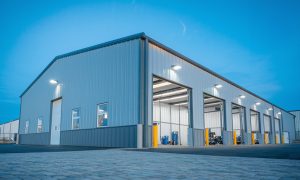 Bolt-up mechanic repair shop metal building being with multiple bay doors, bright interior lighting, and a paved lot.