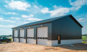 A modern, newly constructed, four car metal building garage with black siding, white overhead doors, on a rural lot