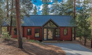 Residential metal buildings with living quarters, red siding, black roof, and full glass entry in a wooded setting
