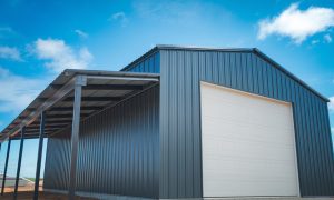 Large steel building parking garage with an attached lean-to canopy shelter on a dirt building lot under blue sky