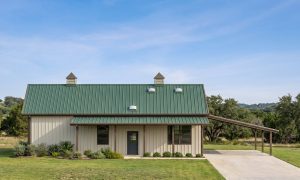 The Grove 50×50 barndominium front elevation (south on the plan), photoreal render: 4:12 gable, the 36 foot front porch and two cupolas