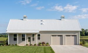 The Meadow 40×60 barndominium front elevation (south on the plan), photoreal render: 6:12 gable, the 24 foot front porch, two cupolas and two overhead doors into the 2-car garage